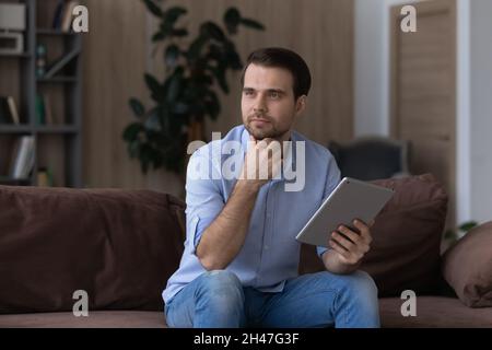 Nachdenklicher junger, gutaussehender Mann mit digitalem Tablet. Stockfoto