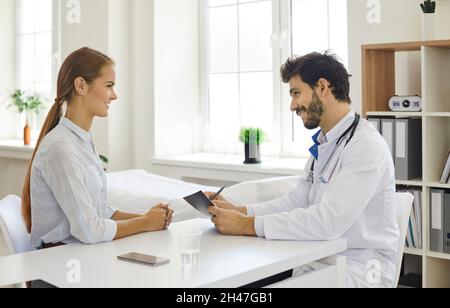 Lächelnder Arzt im Gespräch mit dem Patienten, der am Schreibtisch in seiner Arztpraxis sitzt Stockfoto