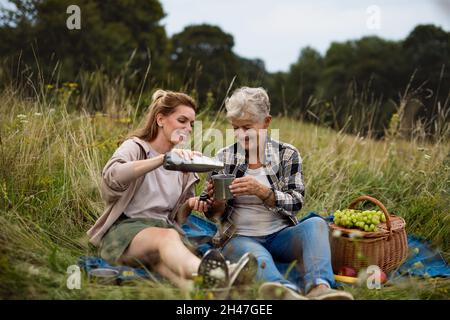 Glückliche ältere Mutter und Erwachsene Tochter sitzen und Picknick im Freien in der Natur. Stockfoto