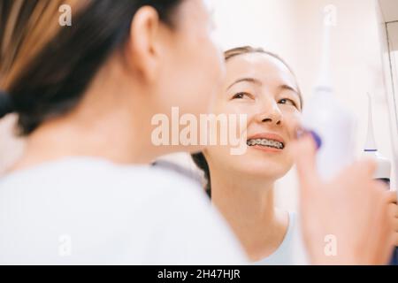 Eine junge Frau mit Zahnspange schaut nach dem Zähneputzen in den Spiegel. Stockfoto