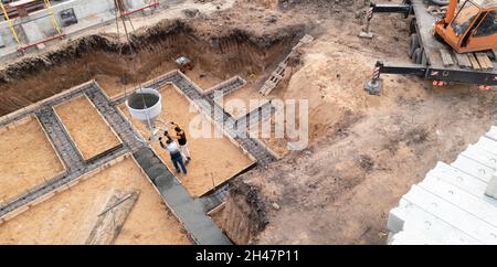 Baustelle mit Arbeitskräften, die Beton in Schalung mit Bewehrung gießen. Feuchter Zement fließt in das Fundament des zivilen Gebäudes, Luftaufnahme. Stockfoto