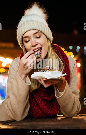 Porträt einer glücklichen jungen Frau, die auf dem weihnachtsmarkt Donuts isst. Urlaub Spaß Menschen Konzept Stockfoto