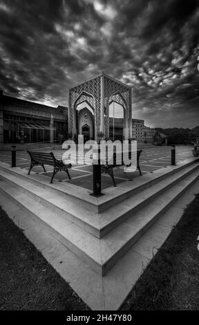 ISLAMABAD, PAKISTAN - 01. Sep 2021: Eine vertikale Graustufenaufnahme eines traditionellen Gebäudes mit Bänken im Vordergrund Stockfoto