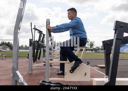 Ein Mann in einem Geschäftsanzug wärmt sich auf Simulatoren im Stadion auf. Sportübungen nach der Büroarbeit. Der Kampf gegen Übergewicht. Geschäftsmann Stockfoto