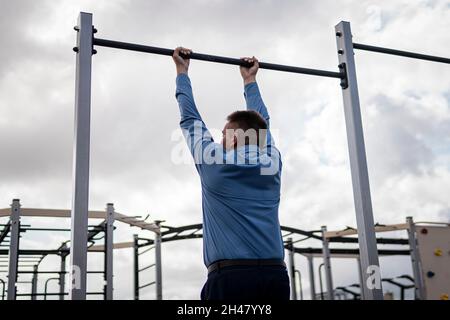 Ein Mann in einem Geschäftsanzug wärmt sich auf Simulatoren im Stadion auf. Sportübungen nach der Büroarbeit. Der Kampf gegen Übergewicht. Geschäftsmann Stockfoto