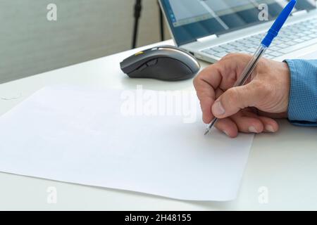 Männliche Hand mit Schreibfeder auf einem leeren Blatt Papier. Platz für Text und Gestaltung kopieren. Eine Hand mit einem Stift in Nahaufnahme kennzeichnet ein leeres Papierdokument. Stockfoto