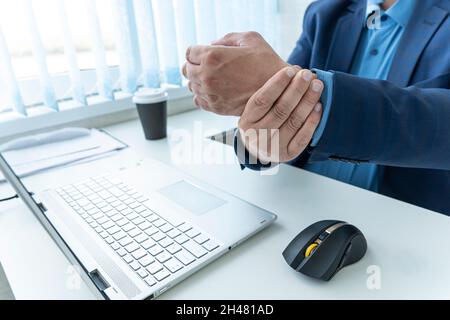Ein Geschäftsmann leidet unter Schmerzen am Handgelenk. Ein Mitarbeiter spürt Schmerzen am Handgelenk, nachdem er lange Zeit an der Tastatur gearbeitet hat. Stockfoto