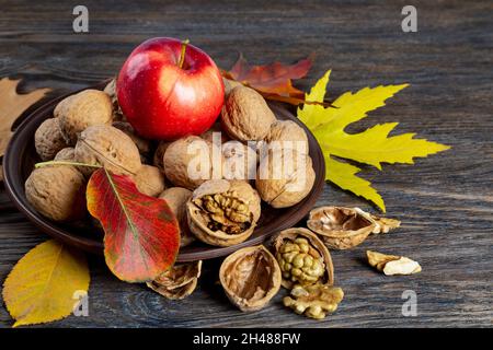 Stillleben im Herbst mit Walnüssen und Apfel. Apfelfrüchte und Nüsse auf braunem Holzhintergrund Stockfoto