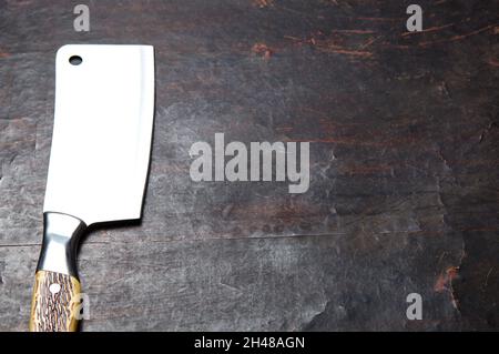 Fleischspalter auf dunklem Holzhintergrund. Küchenmesser oder Metzgerspalter aus Edelstahl auf einer Holzplatte Stockfoto