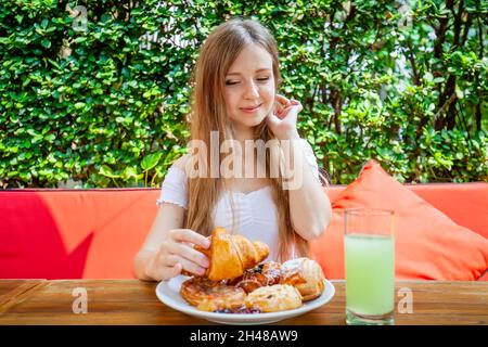 Glückliche Frau essen süßes Frühstück oder Mittagessen im Restaurant im Freien, frisches Gebäck Stockfoto