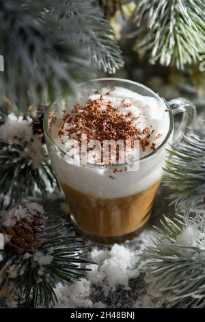 Weihnachtlicher Latte Macchiato. Ein tolles heißes Kaffeegetränk mit Schokoladenragen, zwischen den schneebedeckten Kiefernzweigen und Schnee. Stockfoto