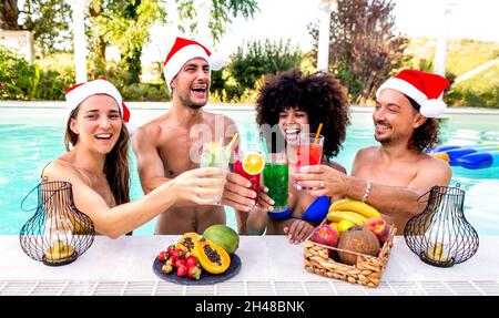 frohe weihnachten! Fröhliche, vielfältige Gruppe von Freunden, die Weihnachtsmütze tragen und Cocktail-Drinks auf der Poolparty genießen, um den Winter zu feiern Stockfoto