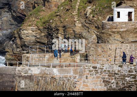 Die Menschen stehen und beobachten die Wellen, die gegen die Klippen krachen, bevor sie bei Flut in Portreath, Cornwall, den Hafen betreten Stockfoto