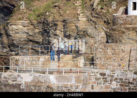 Die Menschen stehen und beobachten die Wellen, die gegen die Klippen krachen, bevor sie bei Flut in Portreath, Cornwall, den Hafen betreten Stockfoto