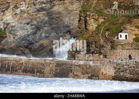 Die Menschen stehen und beobachten die Wellen, die gegen die Klippen krachen, bevor sie bei Flut in Portreath, Cornwall, den Hafen betreten Stockfoto