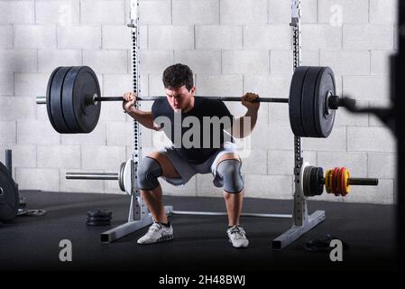 Ganzkörperansicht des jungen Mannes, der Rückenhocken-Übungen in der Turnhalle mit schweren Platten durchführt. Stockfoto