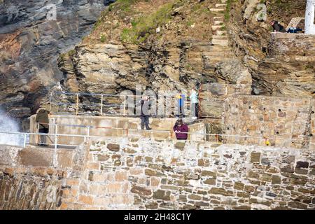 Die Menschen stehen und beobachten die Wellen, die gegen die Klippen krachen, bevor sie bei Flut in Portreath, Cornwall, den Hafen betreten Stockfoto