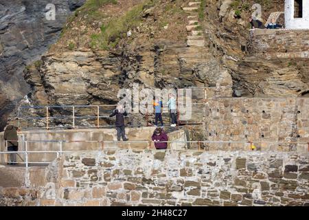 Die Menschen stehen und beobachten die Wellen, die gegen die Klippen krachen, bevor sie bei Flut in Portreath, Cornwall, den Hafen betreten Stockfoto