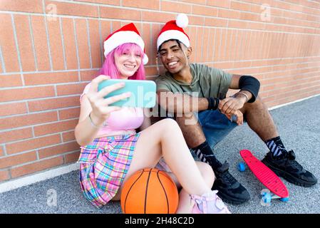 frohe weihnachten! Fröhliche verschiedene paar Freunde tragen weihnachtsmann Hut machen ein Selfie-Porträt sitzen vor einer Hintergrundwand zusammen im Winter Stockfoto