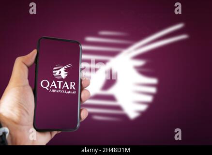 Doha, Katar, Juli 2021: Eine Hand hält ein Telefon mit der Qatar Airways Airline App auf dem Bildschirm und das arabische Oryx-Logo verschwommen auf einem dunklen Kirschbaum-Bac Stockfoto