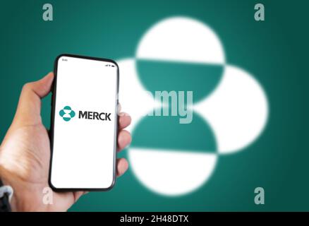 New York, USA, Oktober 2021: Eine Hand hält ein Telefon mit der App des Pharmaunternehmens Merck auf dem Bildschirm und das Merck-Logo verschwimmt auf einer grünen Hintergrundfläche Stockfoto