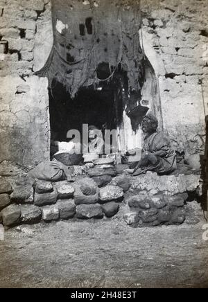 Shuster (?), Iran: Eingang eines Ladens mit zwei älteren Männern in Turbanen, die neben Körben mit Produkten sitzen. Foto, 1910/1920 (?). Stockfoto