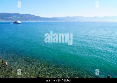 Herrliches türkisfarbenes Wasser des Bodensees mit den Alpen im Hintergrund, von den Ufern der Insel Lindau an einem sonnigen Frühlingstag in G gesehen Stockfoto