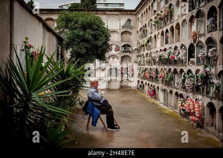 Barcelona, Spanien. 1. November 2021, Barcelona, Spanien: Ein Mann sitzt auf dem Friedhof Poblenou in Barcelona vor mit Blumen geschmückten Gräbern. Der 01. November ist der katholische Feiertag Allerheiligen, der dem Gedenken an die Verstorbenen gewidmet ist. Quelle: Jordi Boixareu/Alamy Live News Stockfoto