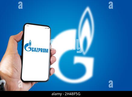 Sankt Petersburg , RUS, Oktober 2021: Hand hält ein Telefon mit der Gazprom Mobile App auf dem Bildschirm und das Logo verschwommen auf einem blauen Hintergrund. Gazpro Stockfoto