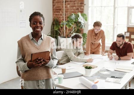 Portrait pof junge schwarze Frau lächelt die Kamera an, während sie im kreativen Designstudio, im Kopierraum arbeitet Stockfoto