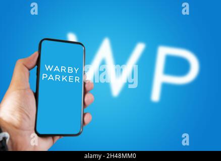 New York, USA, September 2021: Hand hält ein Telefon mit der Warby Parker Mobile App auf dem Bildschirm und das Logo verschwommen auf einem blauen Hintergrund. Warby Pa Stockfoto