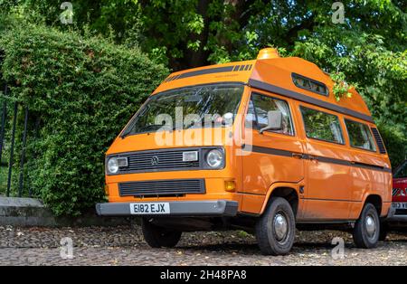 York, Yorkshire, England, 8. Oktober 2021 - Orange Voltswagon T3 Camper Van auf einer Straße mit grünem Laubhintergrund geparkt. Stockfoto