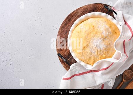 Roher Hefeteig mit Kürbis in weißer Schüssel mit Handtuch auf dem bemehlten Küchentisch bedeckt, Rezeptidee. Konzept Hausbacken Brot, Brötchen oder Cinnabon o Stockfoto