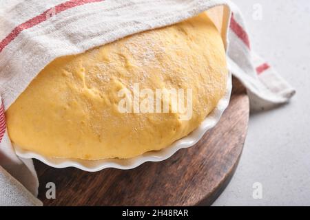 Roher Hefeteig mit Kürbis in weißer Schüssel mit Handtuch auf dem bemehlten Küchentisch bedeckt, Rezeptidee. Konzept Hausbacken Brot, Brötchen oder Cinnabon o Stockfoto