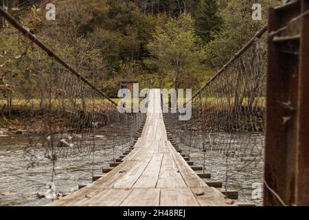 Alte hölzerne Hängebrücke über den Gebirgsfluss im Herbstwald. Moody Image. Hintergrund auf dem Land. Stockfoto