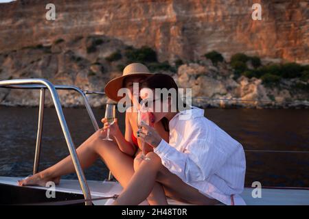 Zwei junge Frauen ruhen sich bei Sonnenuntergang auf einer Yacht im offenen Meer aus. Stockfoto