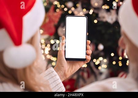 Glückliches Familienpaar in weihnachtsmützen mit Handy-Mockup-Bildschirm an Weihnachten. Stockfoto