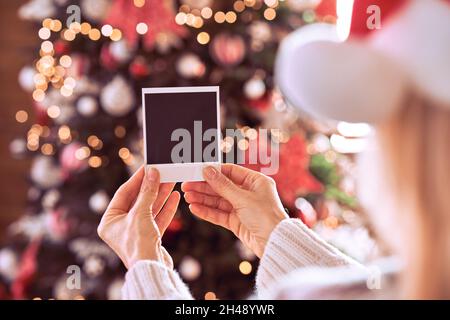 Weibliche Hand hält Weihnachtskarte mit Geschenk auf Weihnachtsbaum Hintergrund. Stockfoto