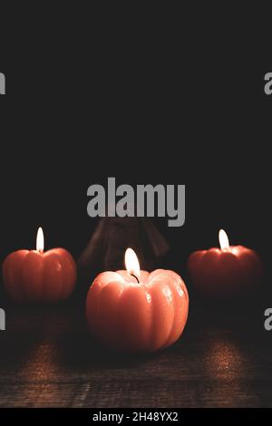 Halloween-thematische Komposition aus drei brennenden Kürbis-förmigen Kerzen mit geisterhaften Figur auf dunklem Hintergrund. Stockfoto