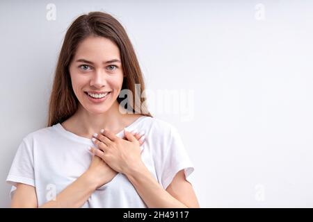 Attraktive glückliche Frau, die Dankbarkeit zum Ausdruck bringt, die Hände auf der Brust hält, für alles dankbar ist, die Kamera mit einem netten Lächeln anschaut, lässig gekleidet Stockfoto