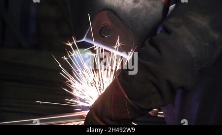 Ein Mann arbeitet mit einer Schweißmaschine. Clip. Schweißen von Stahlkonstruktionen im Werk. Wunderschöne Funken fliegen heraus. Stockfoto