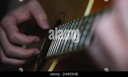 Mann Musiker spielt klassische, akustische Gitarre. Nahaufnahme von männlichen Händen, die Gitarre spielen, im dunklen Raum spielen und Akkorde nehmen, Live-Musik. Stockfoto