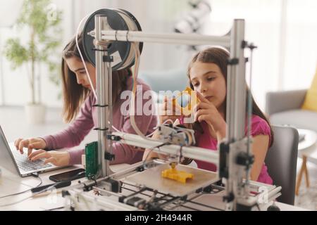 Junge intelligente Mädchen lernen 3D-Druck zu Hause, sie verwenden einen 3D-Drucker und einen Laptop, Wissenschaft und Bildung Konzept Stockfoto