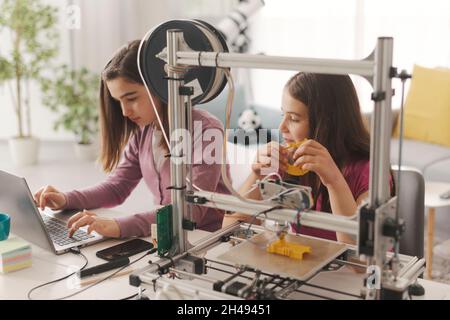 Junge intelligente Mädchen lernen 3D-Druck zu Hause, sie verwenden einen 3D-Drucker und einen Laptop, Wissenschaft und Bildung Konzept Stockfoto