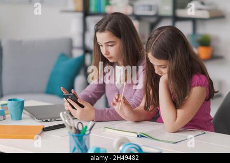 Nette Schülerinnen machen gemeinsam Hausaufgaben, sie sitzen am Schreibtisch im Wohnzimmer Stockfoto