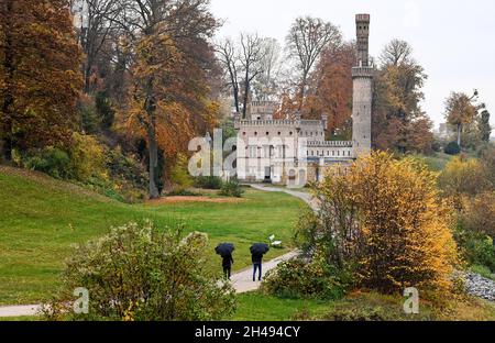 Potsdam, Deutschland. November 2021. Kinderwagen laufen mit Sonnenschirmen am ehemaligen Dampfmaschinenhaus durch den herbstbunten Park Babelsberg. Der November beginnt mit regnerischem Wetter in Berlin und Brandenburg. Das neugotische Backsteingebäude wurde von 1843 bis 45 für die Bewässerungssysteme des Parks errichtet. Quelle: Jens Kalaene/dpa-Zentralbild/ZB/dpa/Alamy Live News Stockfoto