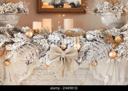 Komposition einer weihnachtsgirlande mit Kerzen, silbernen Kugeln und einem goldenen Bogen am Kamin Stockfoto