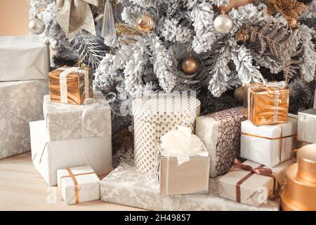 Weihnachtsgeschenke unter einem reich verzierten, schneebedeckten Baum in Pastelltönen Stockfoto