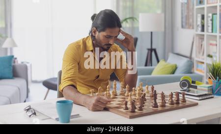 Junger Mann, der am Schreibtisch sitzt und Schach, Strategie und Challenge-Konzept spielt Stockfoto