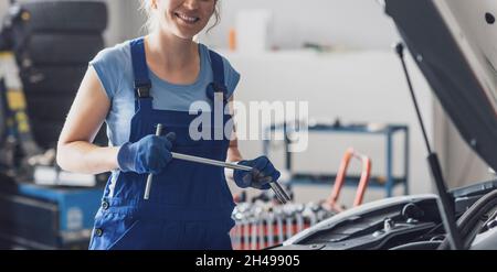 Lächelnde Frau, die in der Autowerkstatt arbeitet, ist eine professionelle Mechanikerin Stockfoto